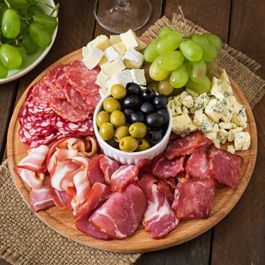 Antipasto catering platter with bacon, jerky, salami, cheese and grapes on a wooden background